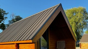 A wooden cabin with a sloped roof, a porch with a chair, and a gravel ground. - Lost Trail Resort (Lava Hot Springs)