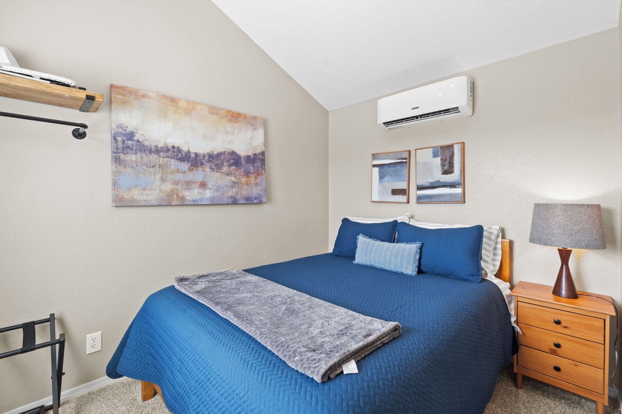 Een slaapkamer met een groot bed, een nachtkastje met een lamp, een airconditioner en kunst aan de muren.