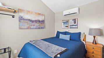 Une chambre à coucher avec un grand lit, une table de chevet avec une lampe, un climatiseur et des œuvres d’art accrochées aux murs.
