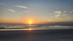 A beach at sunset with the sun low on the horizon, calm sea, and a person standing in the water. - Beach Gear Included! Crisp, Clean & Great Value (Treasure Island)