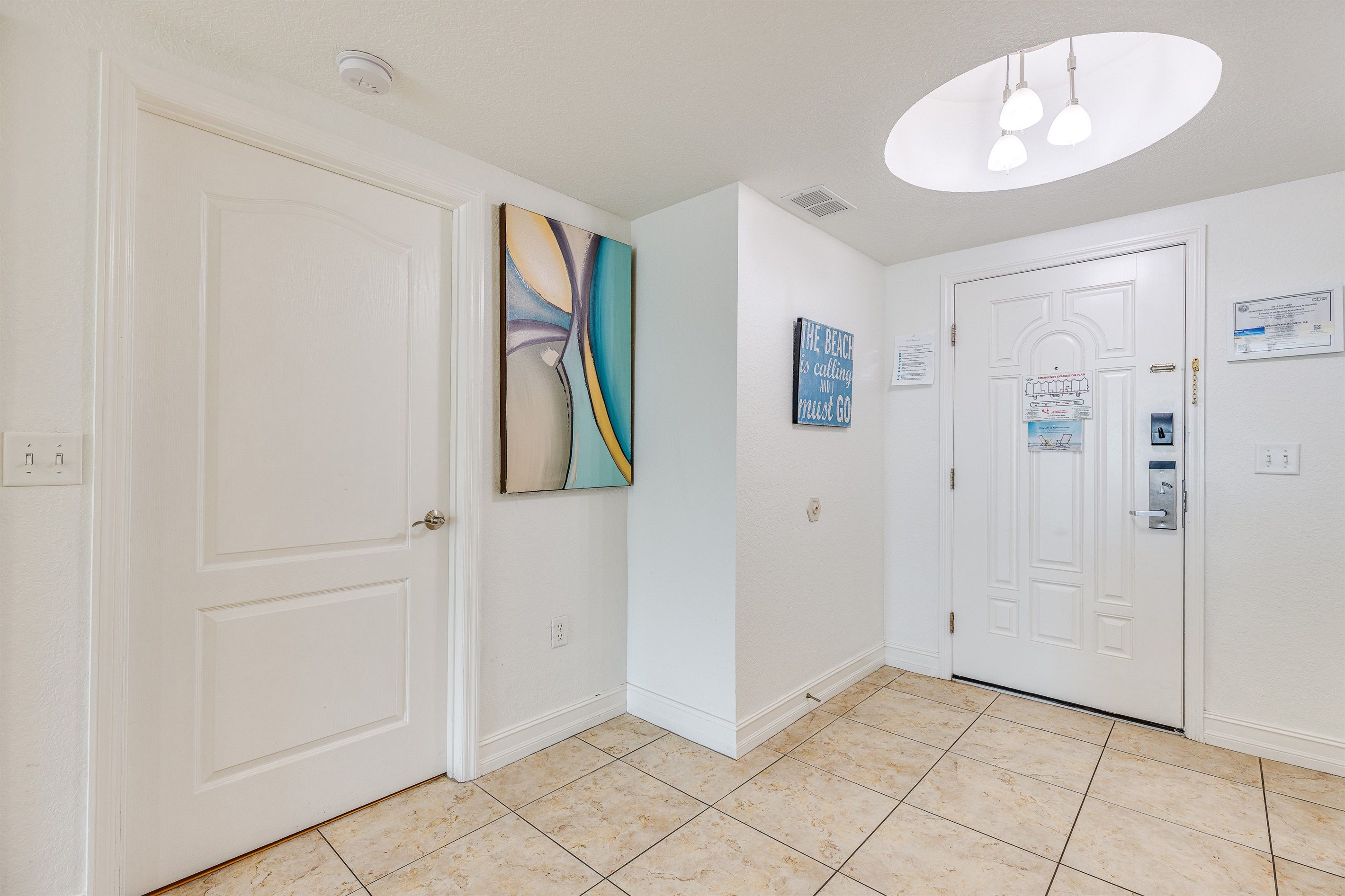A hallway with white walls, a tiled floor, and two white doors. There are wall-mounted light fixtures and a ceiling light.