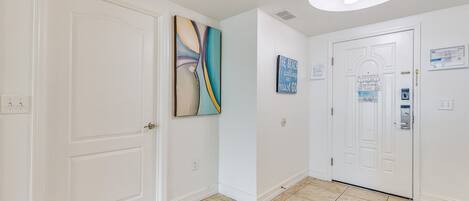 A hallway with white walls, a tiled floor, and two white doors. There are wall-mounted light fixtures and a ceiling light.