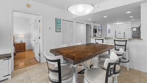 A dining area with a wooden table and four chairs, a chandelier, and a kitchen in the background. - Beach Gear Included! Crisp, Clean & Great Value (Treasure Island)