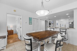 Un coin repas avec une table en bois et quatre chaises, un lustre et une cuisine en arrière-plan.