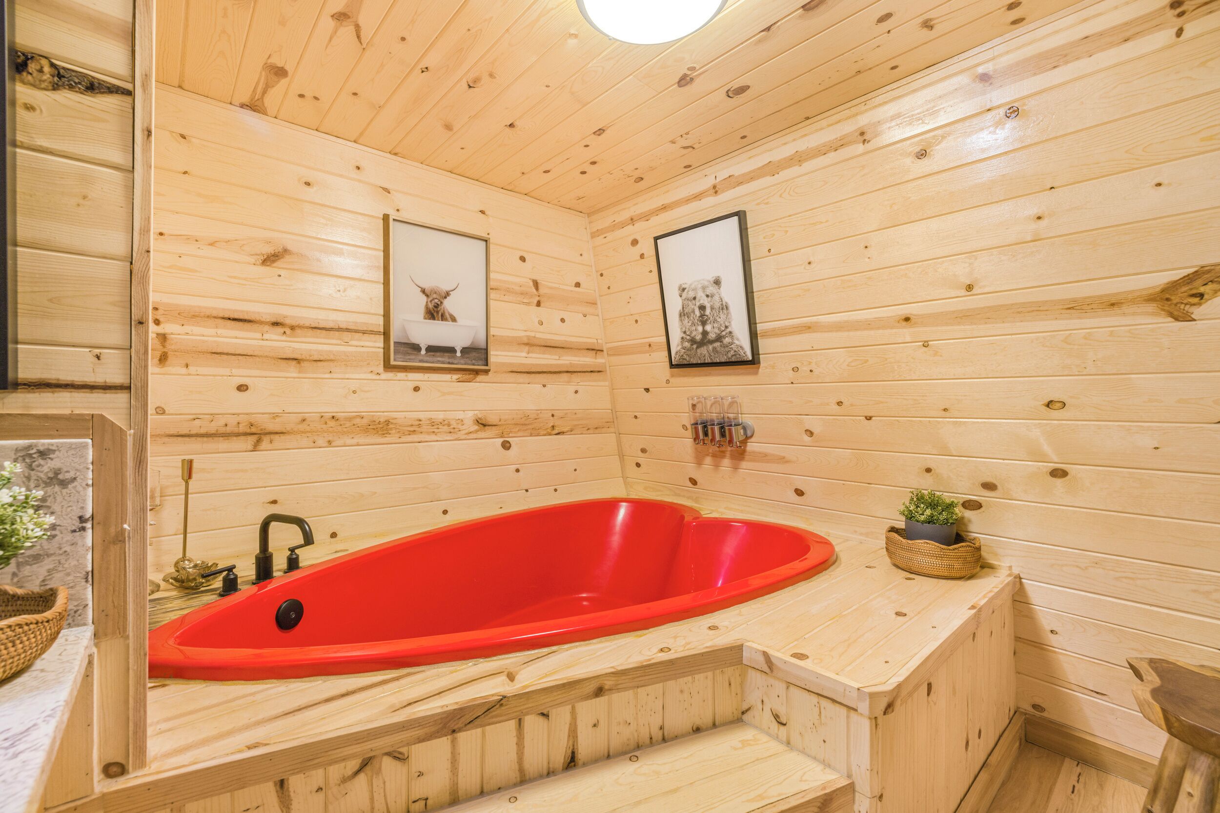 L’intérieur d’un chalet en bois, avec une baignoire rouge, des murs en bois et des tableaux représentant des animaux.