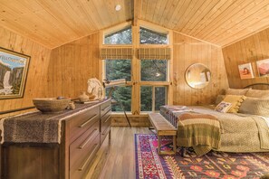 L’intérieur d’une cabane en bois, avec une grande fenêtre, un lit, une commode et un miroir.