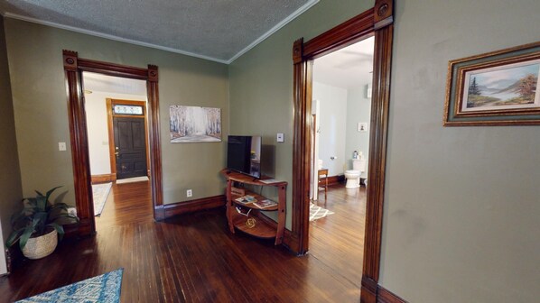 Un salón espacioso con pisos de madera, un televisor sobre un mueble de madera y un cuadro en la pared.
