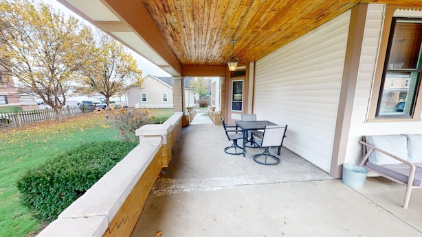 A covered patio with a table and chairs, a concrete floor, and a view of a residential area with houses and trees. - Historic Home in Nelsonville OH near Hocking hills (Nelsonville)