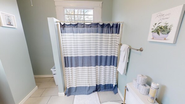 A bathroom with a striped shower curtain, a window, a towel rack, and a framed picture on the wall.