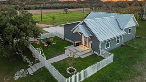 Una casa con techo de metal, patio cercado y un pequeño porche con mobiliario exterior.