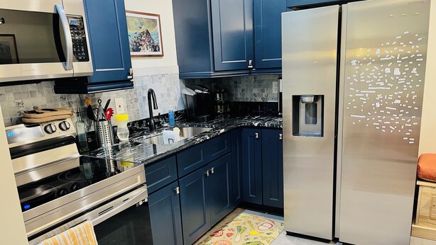 Una cocina moderna con electrodomésticos de acero inoxidable, armarios azul oscuro y un tapete de cocina colorido.