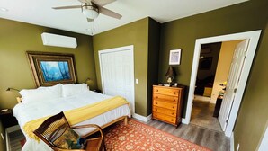 Un dormitorio con una cama, un aparador, una mecedora y una puerta que da a otra habitación.