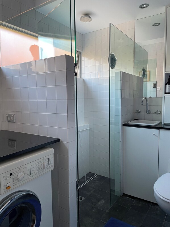 A modern bathroom with a glass shower enclosure, a built-in washing machine, and a sink with a mirror above it.