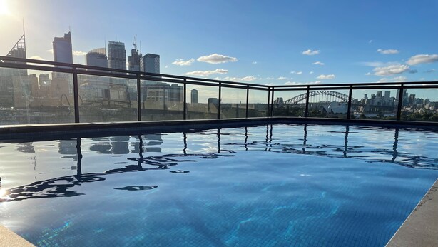 Una piscina de blau clar amb una vista a l'horitzó urbà, incloent un pont al fons.