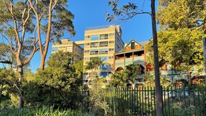 Edifici de diversos pisos amb balcons i zona de jardí amb plantes variades i una tanca.