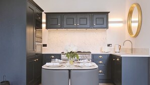 Una cocina moderna con armarios oscuros, un salpicadero de mármol y una mesa redonda para cuatro comensales.