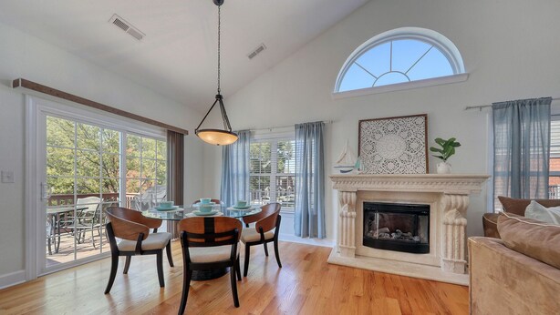 A spacious living room with a fireplace, a dining area with chairs and a table, and large windows offering a view of the outdoors. - Walk to the Beach with Pool and Game Room (Myrtle Beach)