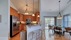 A modern kitchen with wooden cabinets, stainless steel appliances, and a central island with stools. - Walk to the Beach with Pool and Game Room (Myrtle Beach)