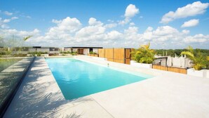 Ein moderner Pool auf dem Dach mit klarem, blauem Wasser, umgeben von einem Holenzaun und viel Grün.