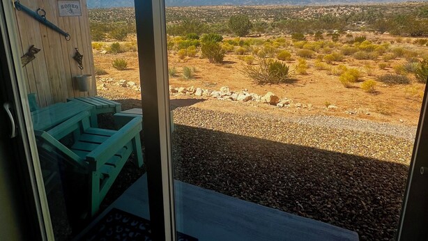 Ein Zimmer mit großem Fenster und Blick auf eine Wüstenlandschaft mit Bergen im Hintergrund.