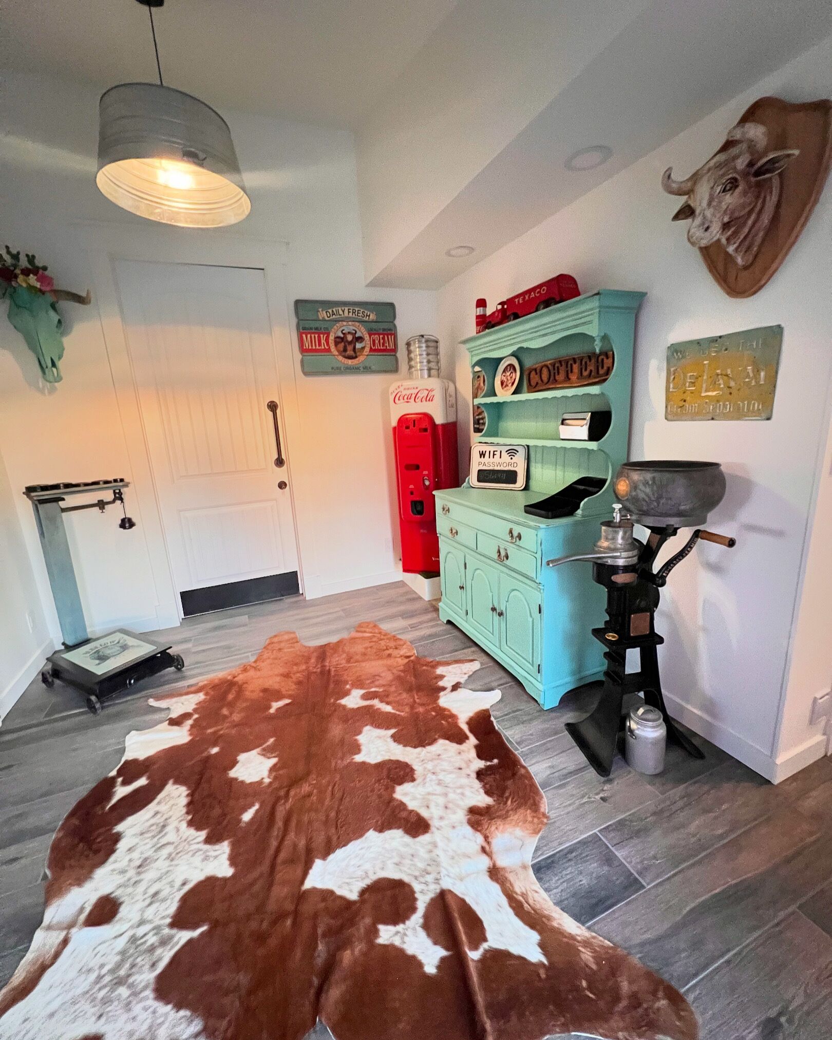 A room with a cowhide rug, a vintage Coca-Cola fridge, a coffee grinder, and a wall-mounted sign reading "Daily Fresh Milk & Cream".