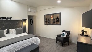 Ein modernes Schlafzimmer mit einem großen Bett, einer Bank, einem Sessel, einem an der Wand montierten Regal mit Laternen und einer Nähmaschine auf einem Nachttisch.