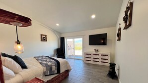 Ein Schlafzimmer mit Bett, Kommode, Fernseher und Blick ins Freie.