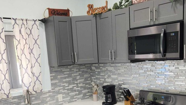 A modern kitchen with grey cabinets, a built-in microwave, a stove, and a coffee maker. - Charming 2-bedroom apartment with WiFi, AC in fantastic eastern Nassau (Nassau)