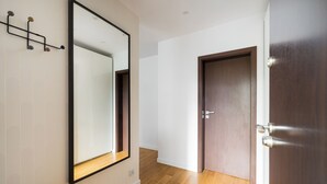 A hallway with a wooden floor, a large mirror, and a wooden door. - Metro Stokłosy 2-Bedroom Apartment (Warszawa)