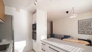 A modern kitchen with white cabinets, a built-in oven, and a large island with a light-colored countertop. - Metro Stokłosy 2-Bedroom Apartment (Warszawa)