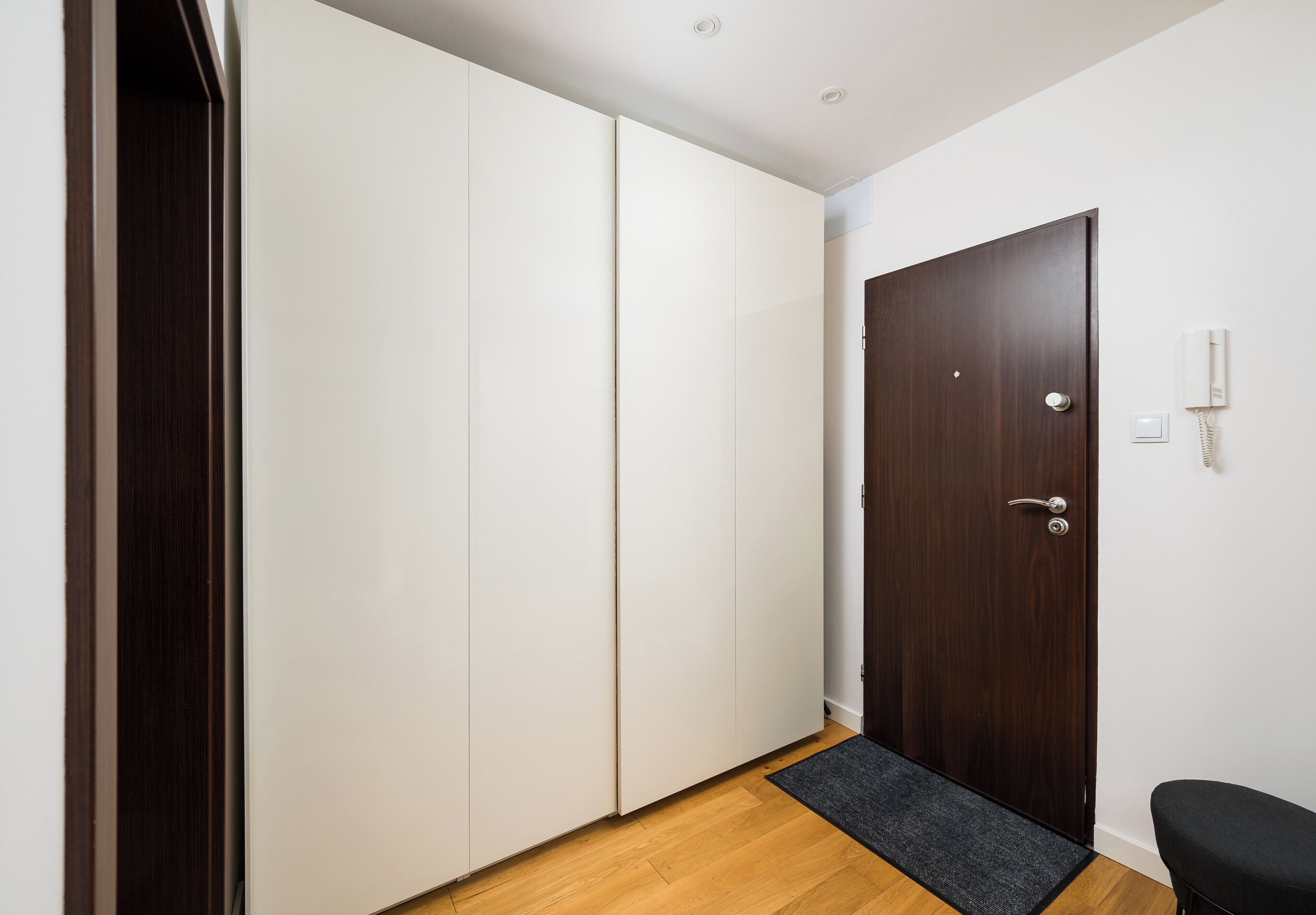 A hallway with a wooden floor, a dark wooden door, and a white wardrobe.