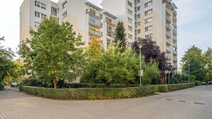 A multi-story residential building with balconies, surrounded by well-maintained hedges and trees. - Metro Stokłosy 2-Bedroom Apartment (Warszawa)