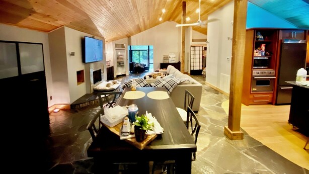 Una cocina moderna con horno y refrigerador integrados, un comedor con mesa y sillas de madera, y una sala de estar con sofá y chimenea.
