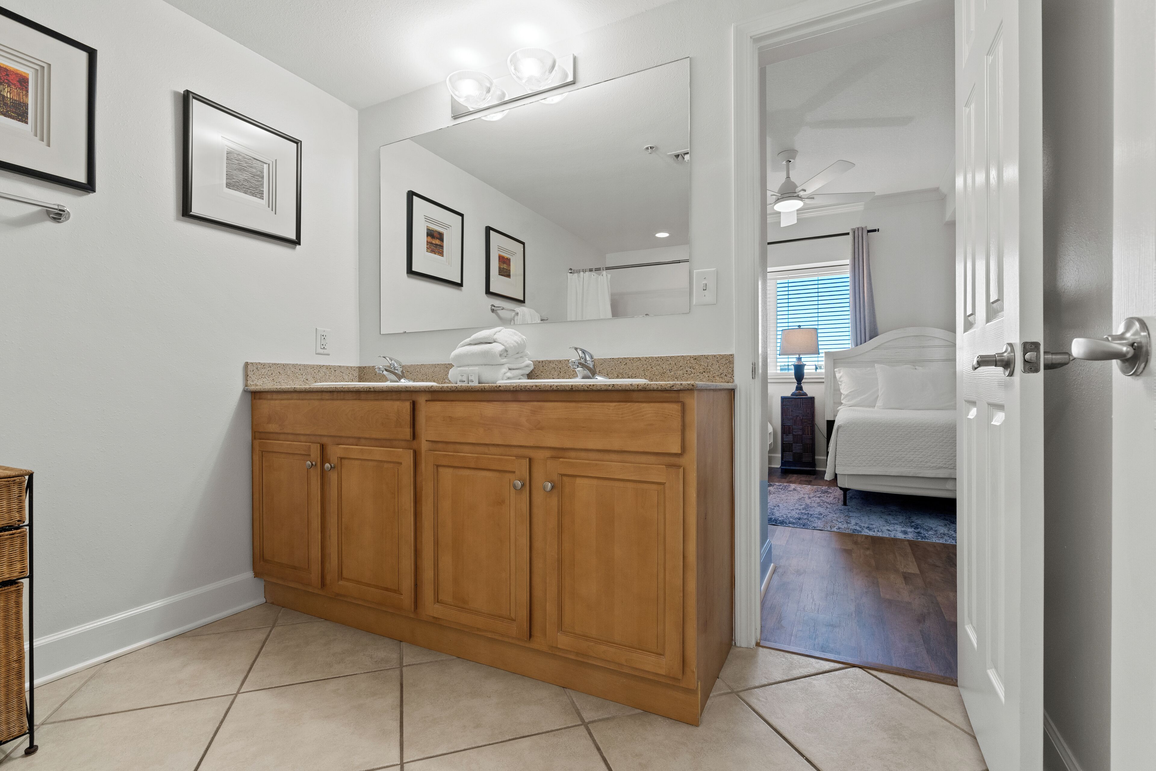 A bathroom with a wooden vanity, a large mirror, and a door leading to a bedroom.