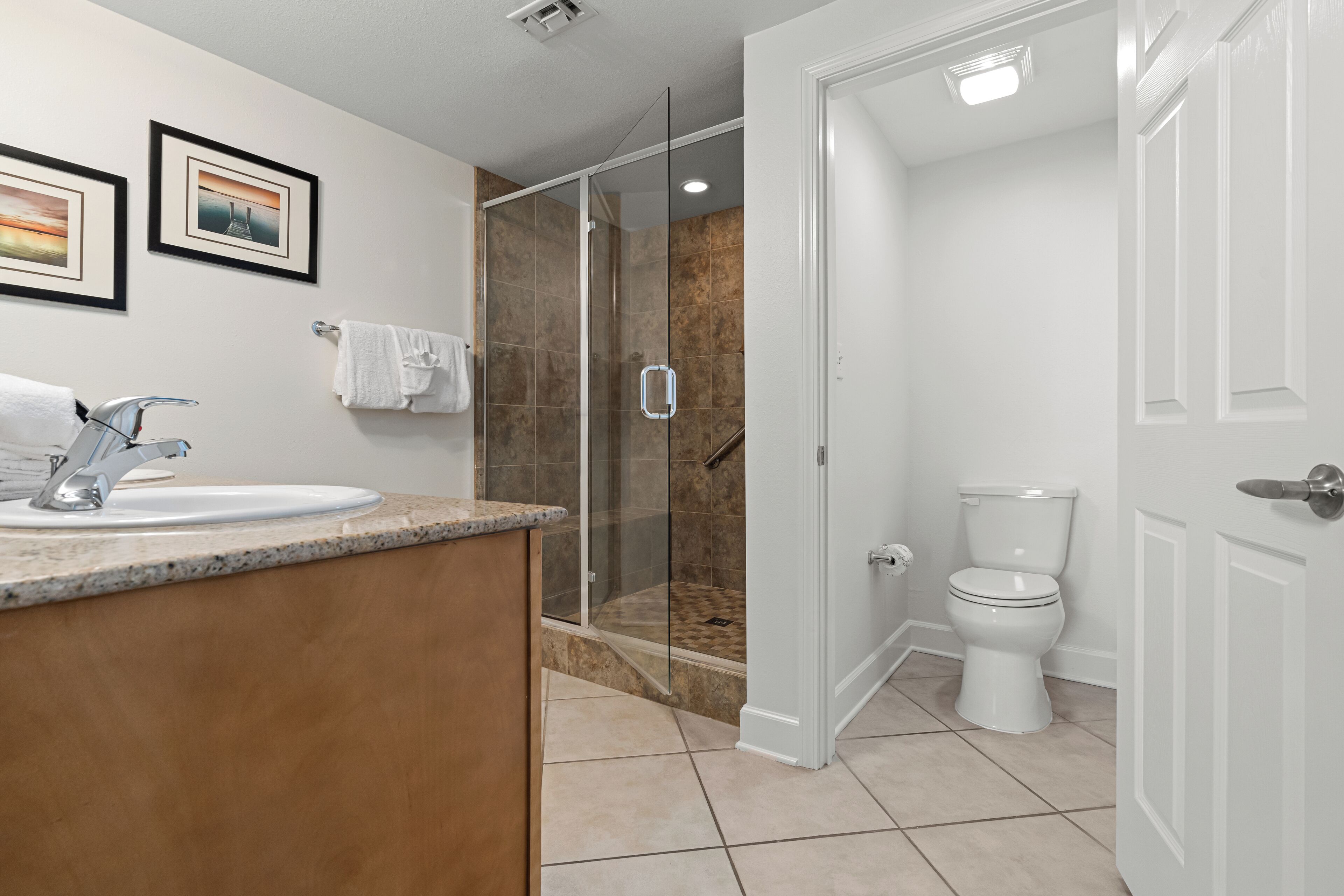 Un baño moderno con cabina de ducha de vidrio, un inodoro blanco y un lavamanos con encimera de granito.