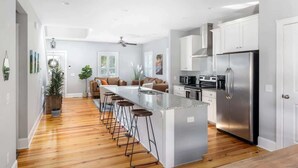 A modern kitchen with a central island, bar stools, stainless steel appliances, and a wooden floor. - Cozy Charleston Home with Putting Green (N. Charleston)