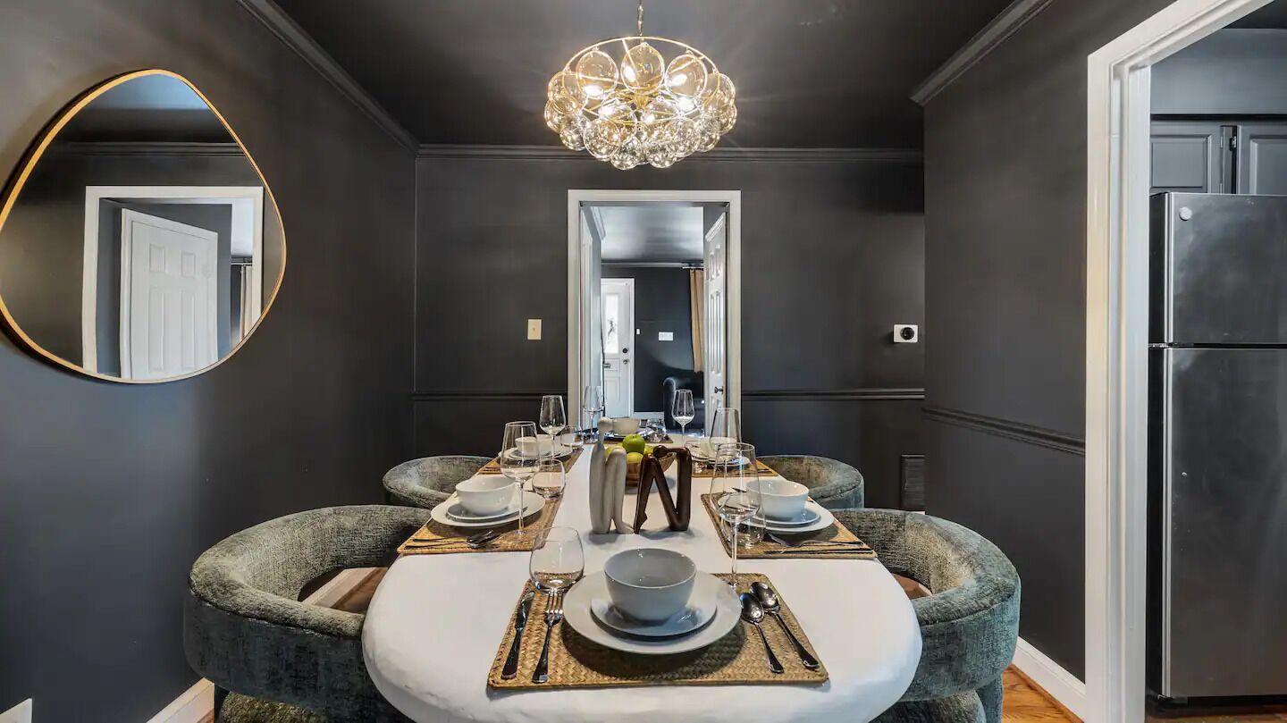 A dining area with a round table set for four, a chandelier, and a large mirror on the wall.