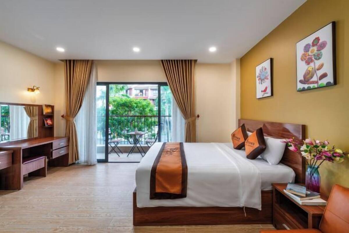Une chambre d’hôtel comprenant un lit, un bureau et une chaise, un balcon avec une table et des chaises, et des œuvres d’art accrochées aux murs.
