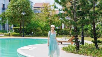 A woman standing by a pool with a clear view of a building in the background.