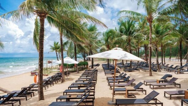 A beach with rows of sun loungers and umbrellas, palm trees, and the ocean in the background. - Luxy Park Hotel & Apartments - MTown (Phu Quoc Island)