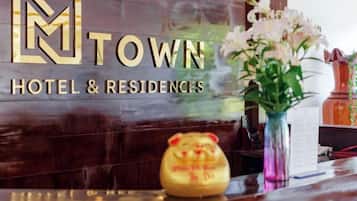 A reception desk with a 'TOWN HOTEL & RESIDENCES' sign, a vase with flowers, and a decorative piggy bank.