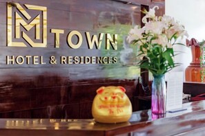 Una mesa de recepción con un letrero que dice 'TOWN HOTEL & RESIDENCES', un florero con flores y una alcancía decorativa.
