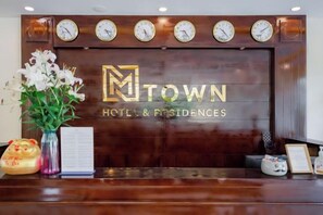 A reception desk with a wooden panel, clocks, and a logo for 'TOWN HOTEL & RESIDENCES'. - Luxy Park Hotel & Apartments - MTown (Phu Quoc Island)