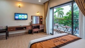 A hotel room with a bed, a TV mounted on the wall, a desk with a chair, and a balcony with outdoor seating. - Luxy Park Hotel & Apartments - MTown (Phu Quoc Island)