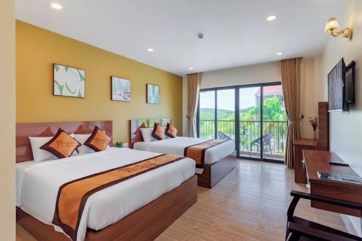 Une chambre d’hôtel avec deux lits, un bureau et un balcon donnant sur un espace verdoyant.