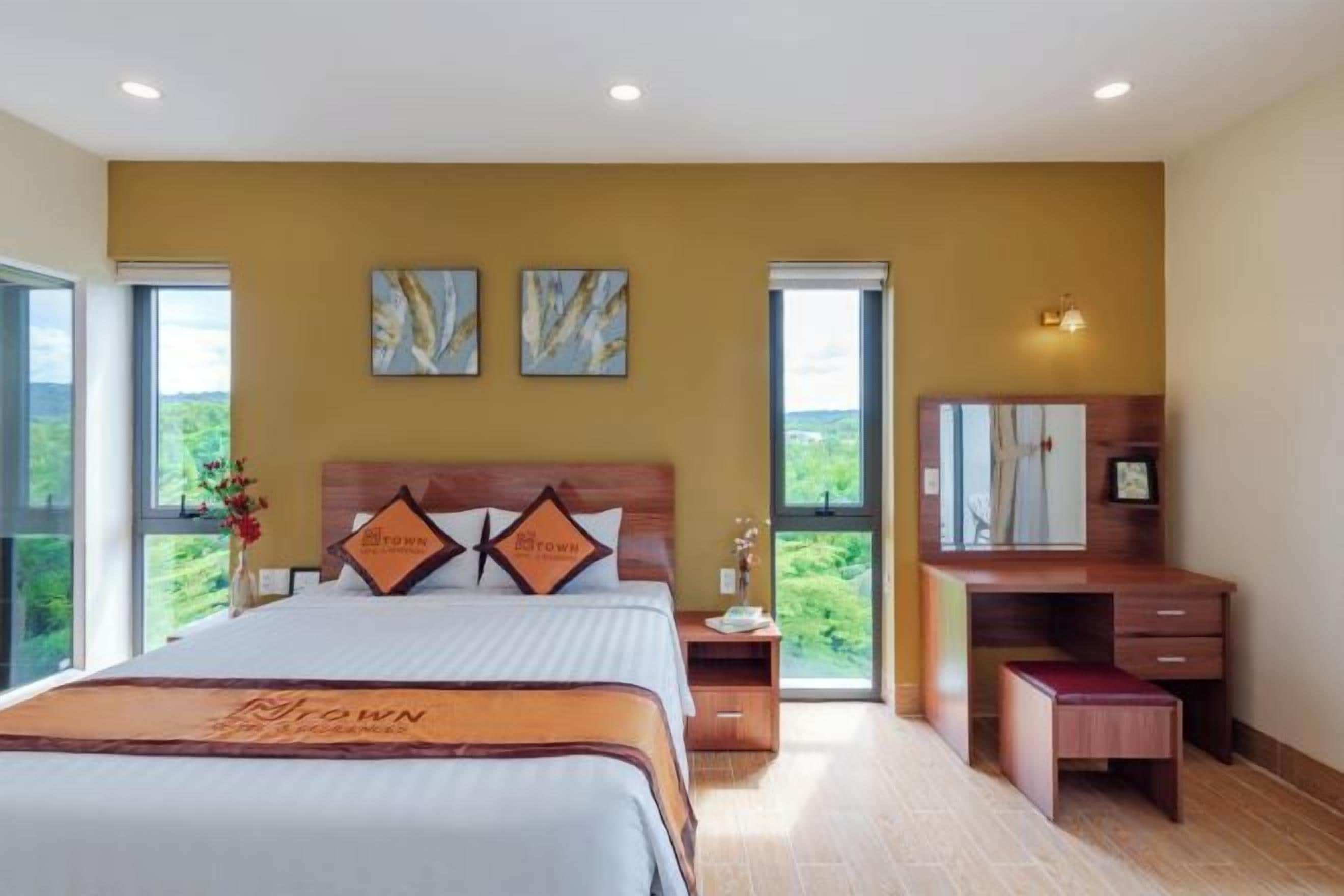 A bedroom with a large bed, a wooden dresser, a nightstand, and a window with a view.