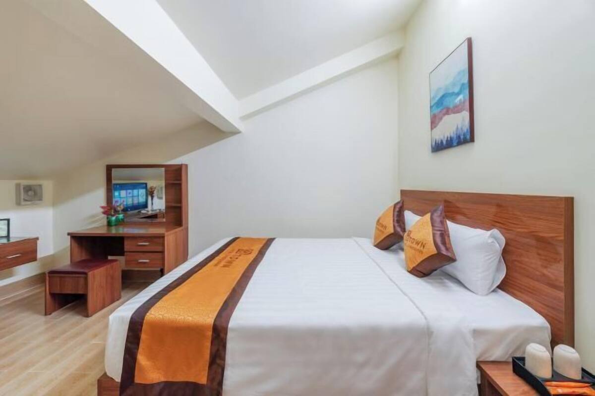Une chambre d’hôtel avec un lit, une tête de lit en bois, un bureau avec une chaise, un petit tabouret et une table de chevet avec des bougies.