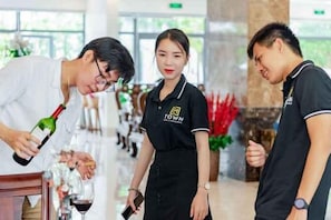 Un hall d’hôtel avec un comptoir d’accueil, une personne en train de servir du vin et un membre du personnel en uniforme.