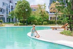A person sitting by a pool with a lounge chair and a building in the background. - Luxy Park Hotel & Apartments - MTown (Phu Quoc Island)