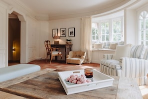 Un salón acogedor con una mesa de centro de madera, sillones a rayas, un sillón de mimbre y vistas al exterior a través de amplios ventanales.